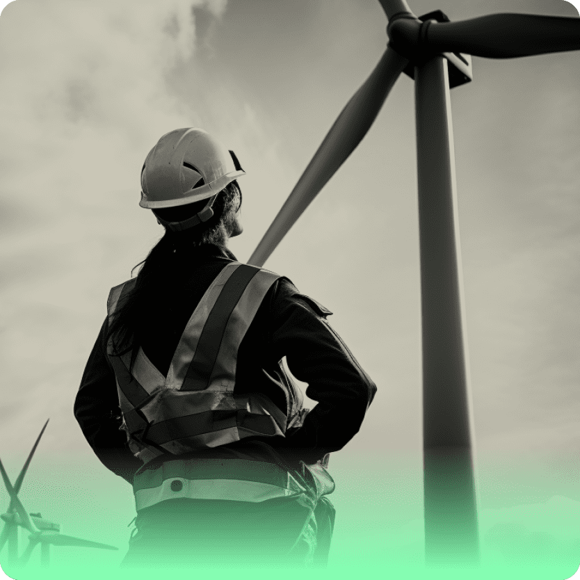 a person looks at a wind turbine, they are wearing safety gear and a hard hat